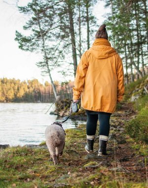 Suvi koiran kanssa järven rannalla kävelemässä poispäin kamerasta.