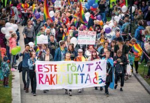 Helsinki Pride kulkue Esteetöntä rakkautta -tekstilakanan kanssa, jossa pyörätuolin kuva.