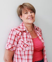 Kirjoittaja Marianne Pentikäinen katsoo iloisesti hymyillen kameraan päällään kirkkaan vaaleanpunainen pusero.
