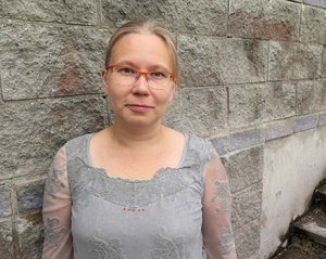 Anne Kallio harmaan kiviseinän edustalla.