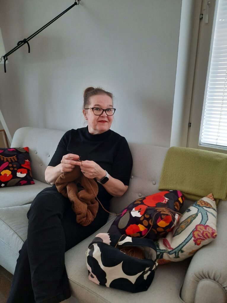 Tummatukkainen nainen istuu sohvalla neulomassa