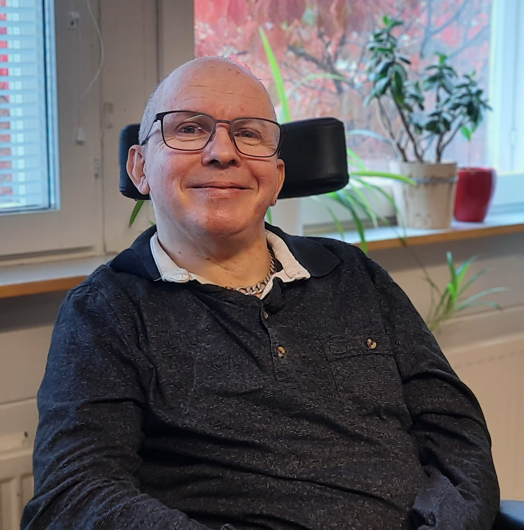 Mies istuu pyörätuolissa hymyillen ikkunan ääressä.