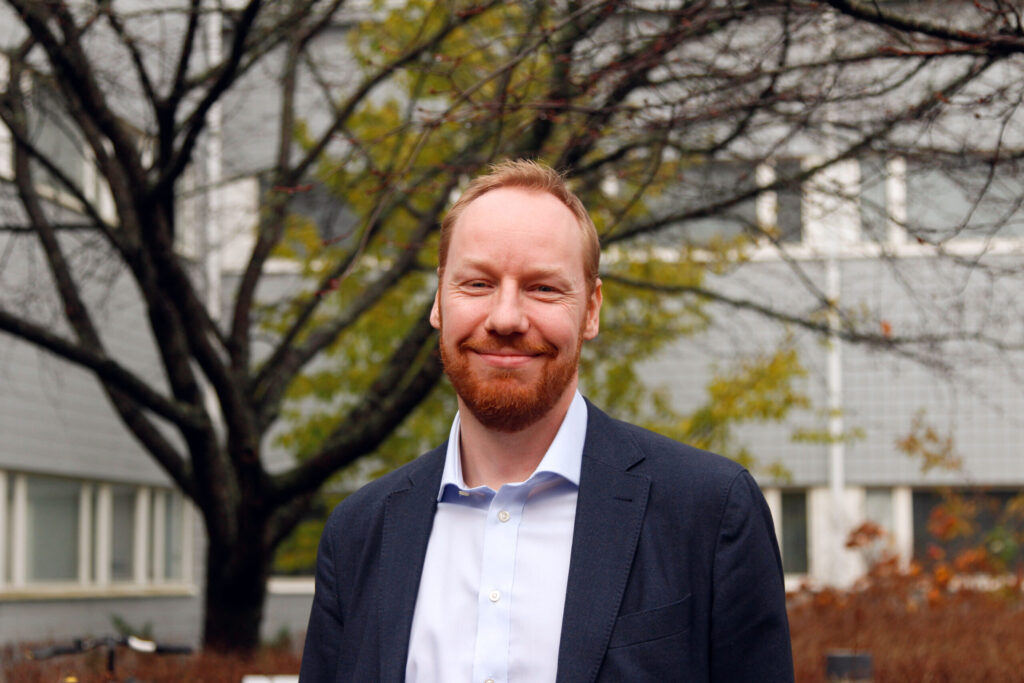 Mies päällään vaaleansininen kauluspaita ja tumman sininen puvuntakki.