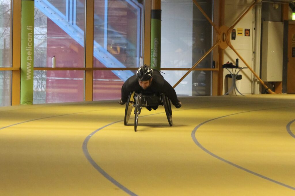 Henkilö kelaa pyörätuolilla sisähallissa.