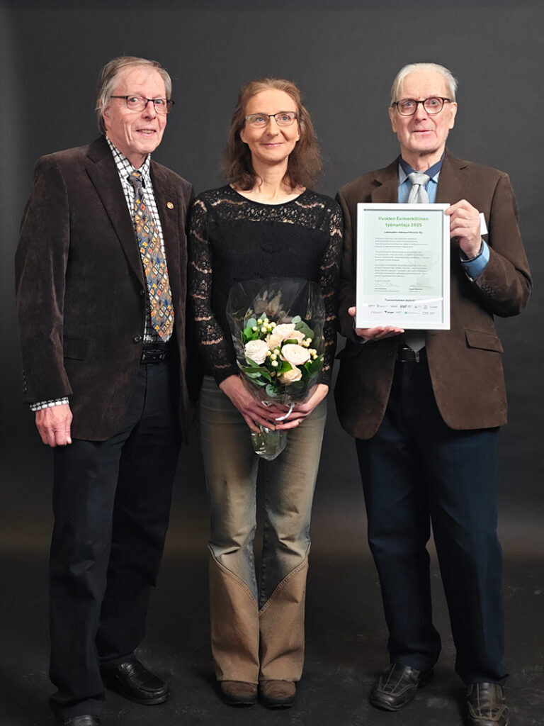 Kolme henkilöä Lakeuden Elämysliikunta ry:stä iloitsee kuvassa palkinnosta. Kaksi miestä ja keskellä nainen, jolla on kukkakimppu kädessään. Oikeanpuoliselle miehellä on diplomi kädessään ja näyttää siltä kameralle. 