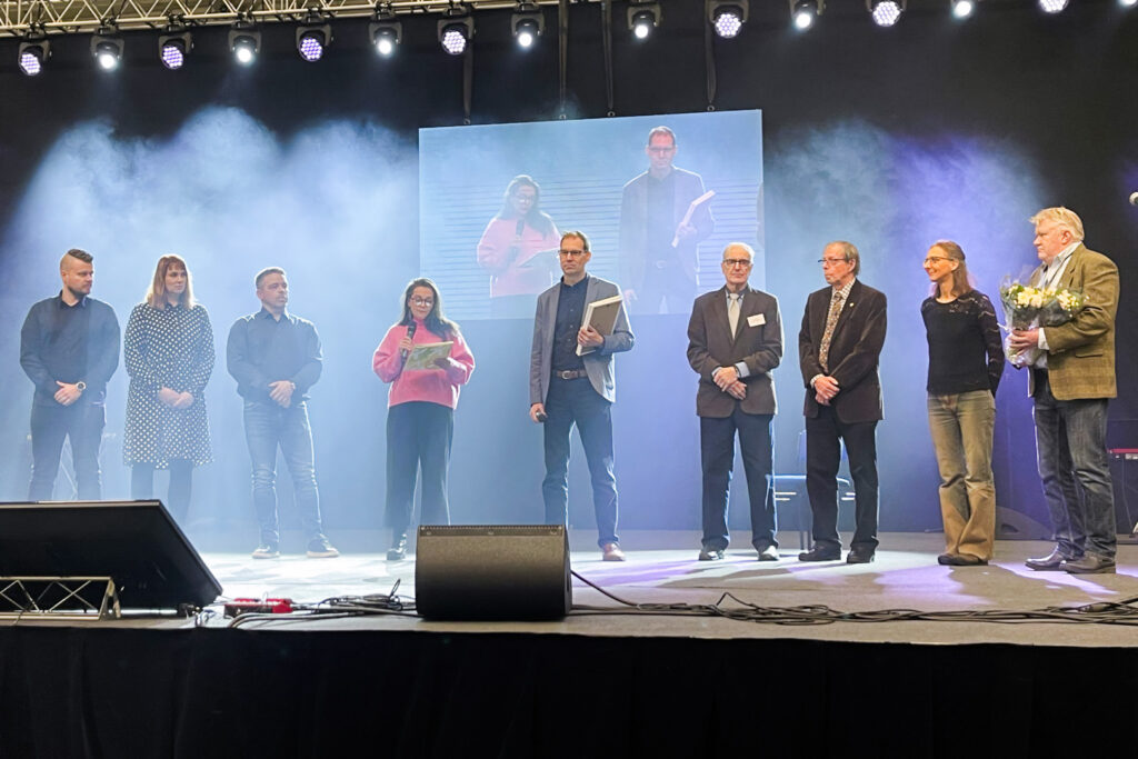 Henkilöitä seisomassa savun peittämällä lavalla.  