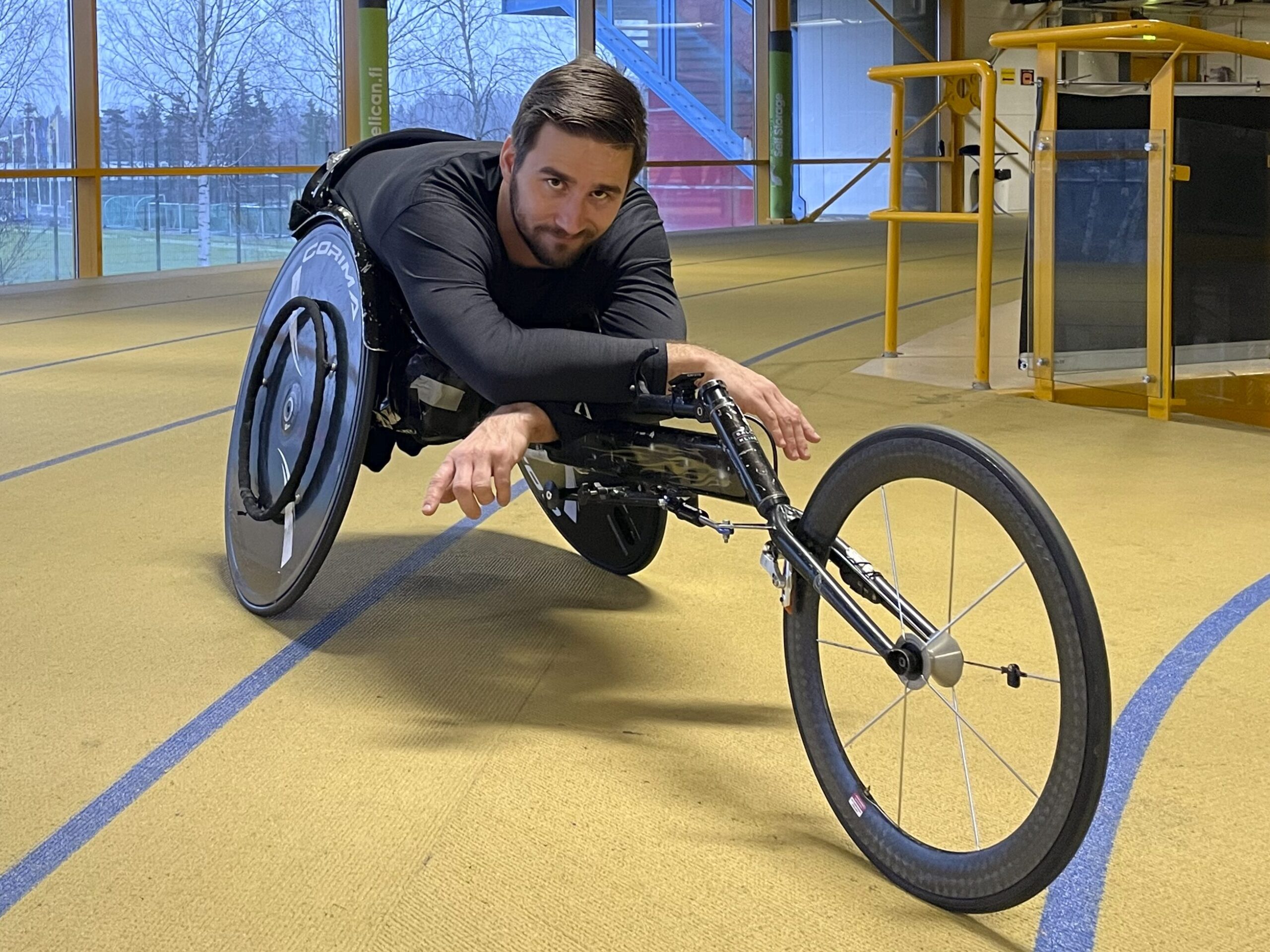 Henkilö istuu ratakelaus pyörätuolissa sisähallissa.