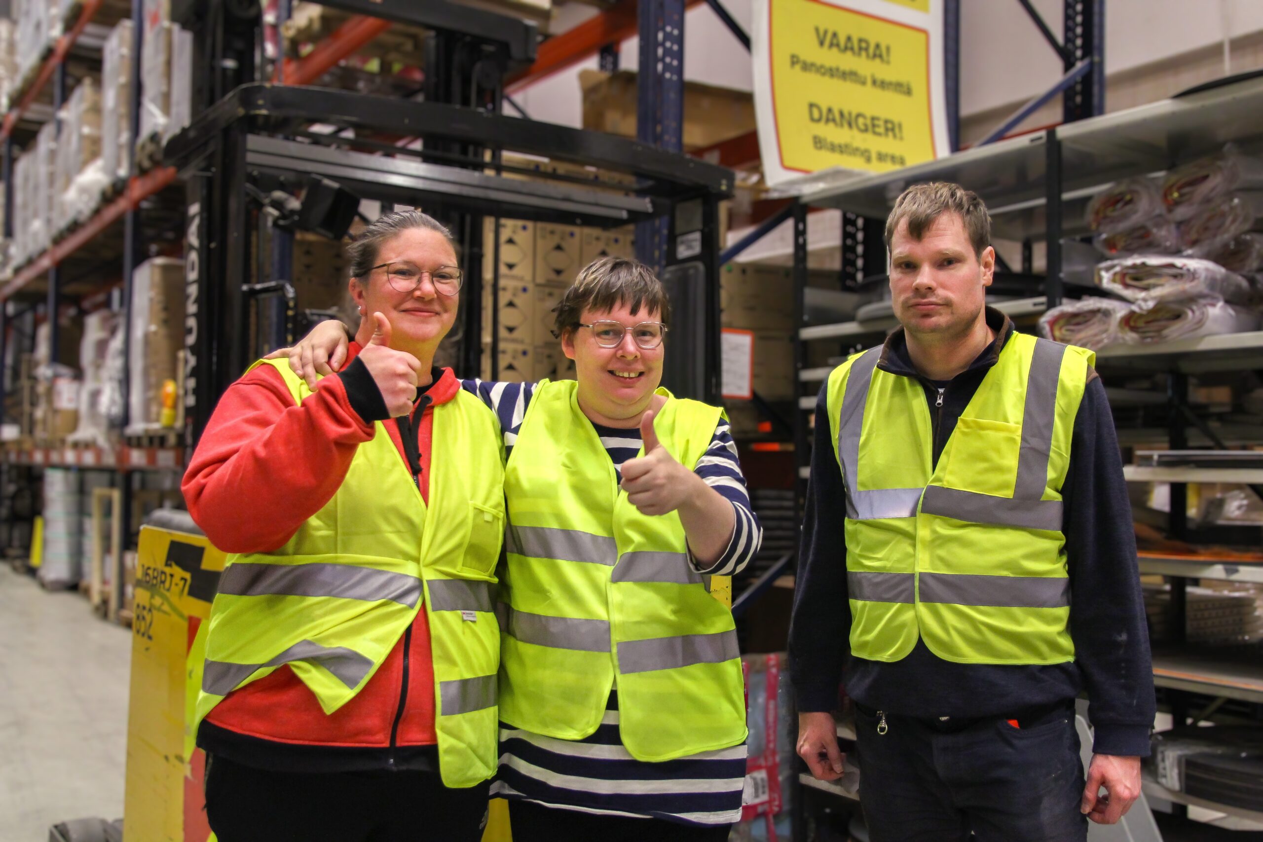 Kolme ihmistä hymyilemässä ja näyttämässä peukkua suojaliivit päällä.