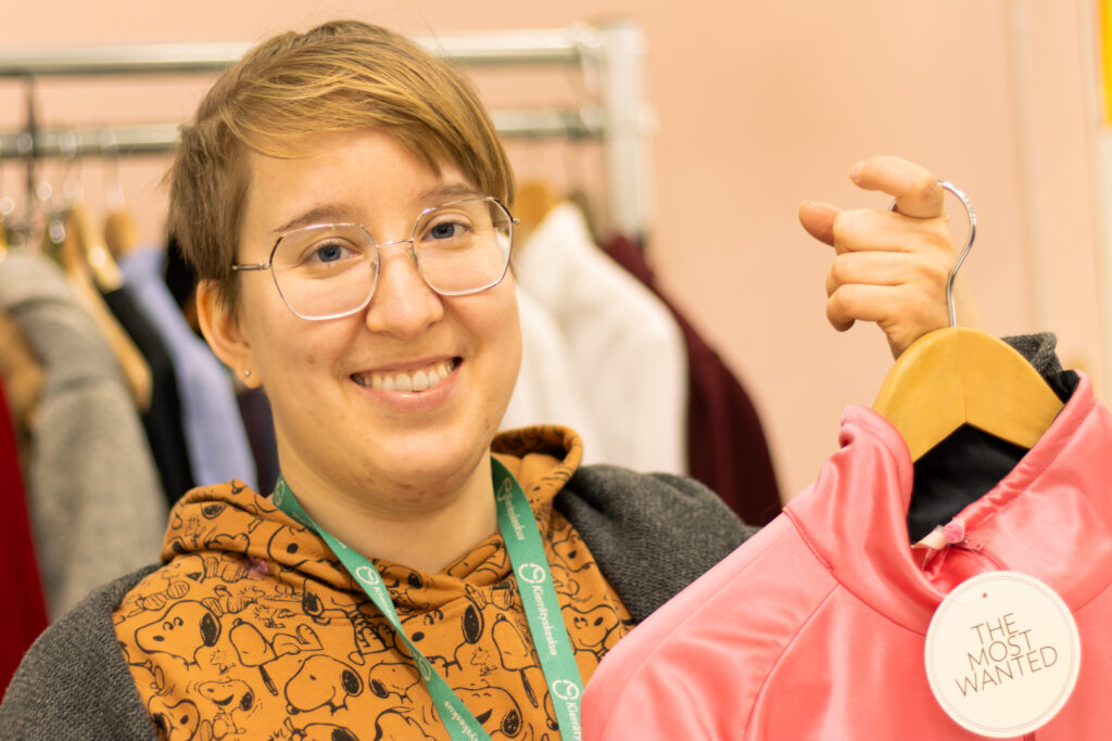 Henkilö hymyilee ja pitelee vaatekappaletta.