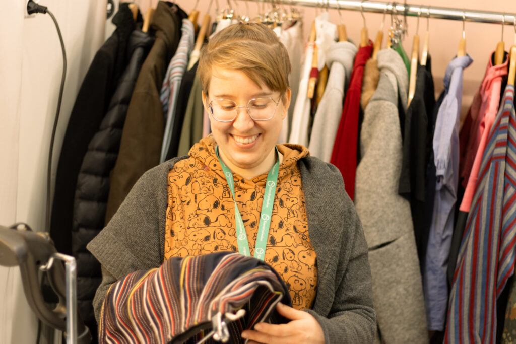 Henkilö seisoo vaaterekin edessä Kierrätyskeskuksen vaatehuoltoverstaalla