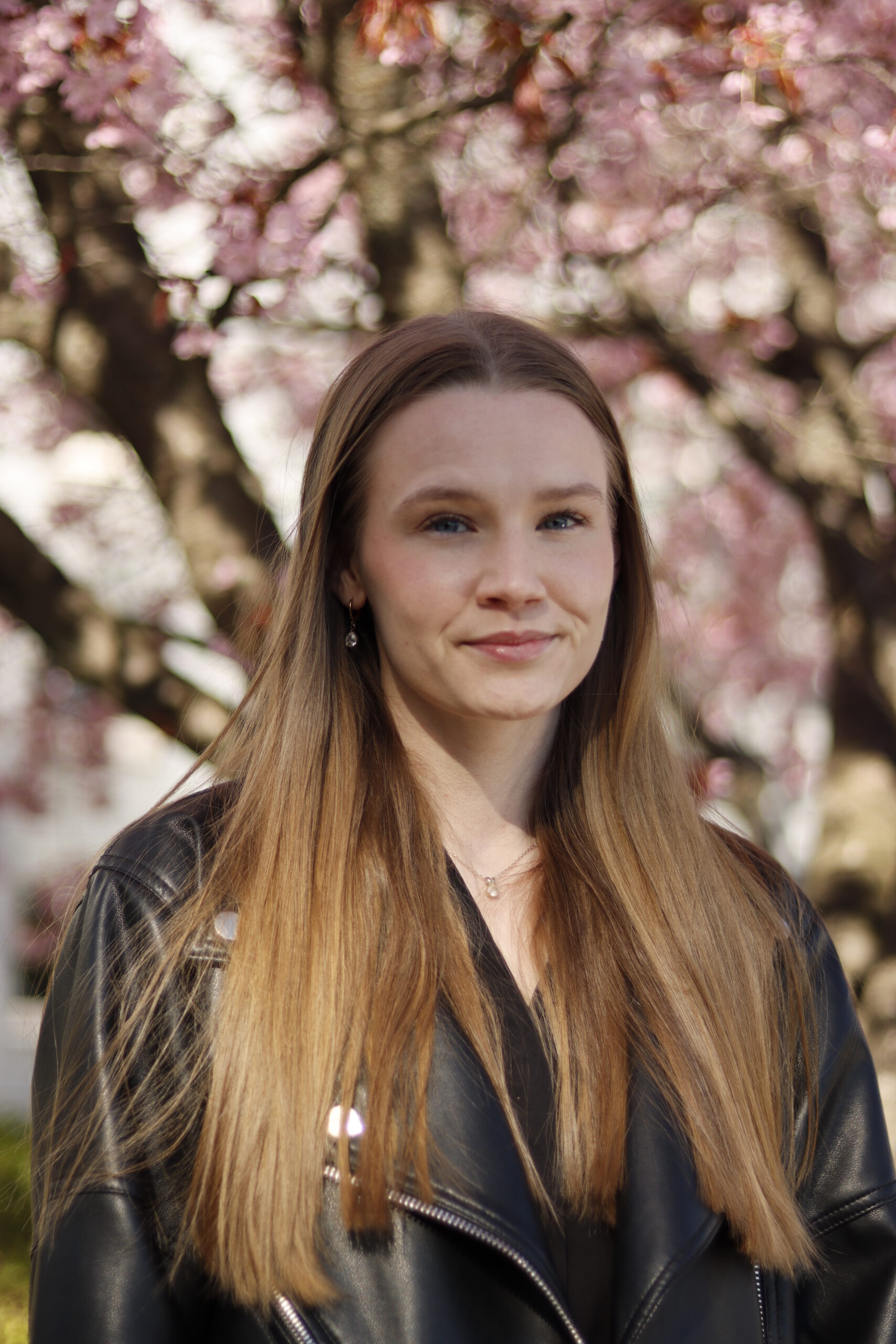Jasmine vaaleat pitkät hiukset ja nahkatakki hymyilee kirsikkapuut taustalla.