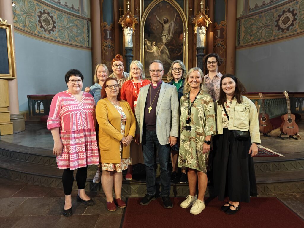 Iso ryhmä henkilöitä kirkossa alttaritaulu taustalla. 