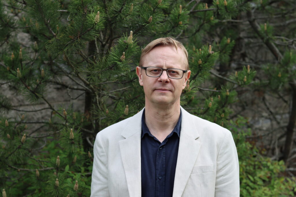Henkilö valkoisessa takissa kesäisessä puistossa.