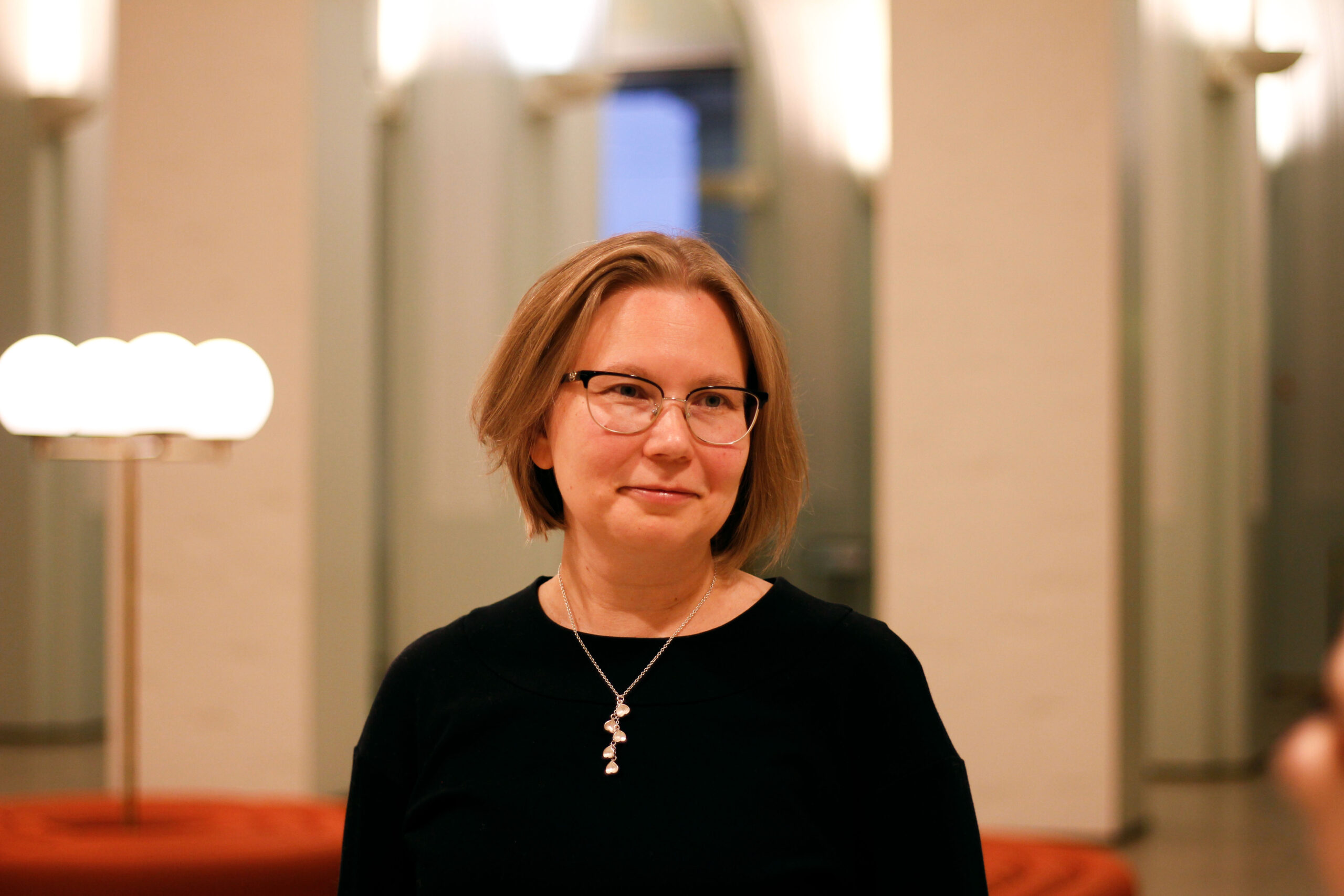 Anne hymyilee kameran edessä, mustassa paidassa.