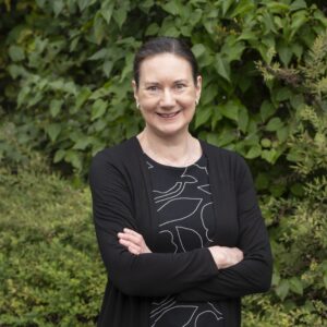 Päivi katsoo kameraan ja hymyilee kesäisessä puistossa.